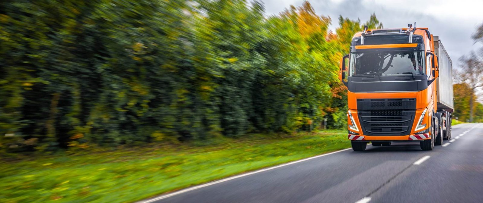 An orange truck driving on a tree-lined road